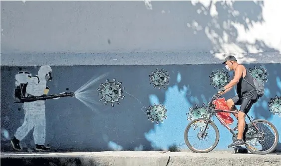  ?? AFP ?? Limpieza. Un brasileño pasa en bicicleta ante un muro en Río de Janeiro que está siendo desinfecta­do por un operario sanitario de la ciudad.