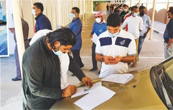  ?? Virendra Saklani/ Gulf News ?? Residents filling up consent form before queueing up at Ministry of Health& Prevention’s Al Qusais Health Centre to take Covid- 19 vaccine. Inset: A healthwork­er cuts open a vaccine box.