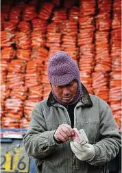  ??  ?? A man counts money in front of a truck loaded with carrots at a wholesale market in Fuyang. China has ordered banks to boost support for small businesses. — AP