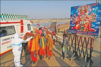  ??  ?? A health worker takes nasal swab samples of Hindu holy men to test for covid-19 next to a poster of Hindu deity Hanuman.