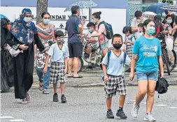  ?? ROSLAN RAHMAN AFP VIA GETTY IMAGES ?? Children walk home with their guardians after school in Singapore on May 17, 2021, as the country prepares to shut all schools and switch to home-based learning until the end of the term due to a rise in the number of COVID-19 cases.