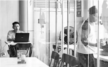  ?? — AFP photo ?? A man (left) uses his laptop at a cafe in Jakarta.