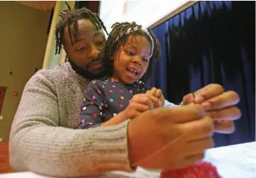  ?? ARKANSAS DEMOCRAT-GAZETTE FILE PHOTO ?? Willie Mooney helps his daughter, Olivia, 4, tie a beaded necklace she made during the Kwanzaa celebratio­n at the Mosaic Templars Cultural Center in Little Rock.