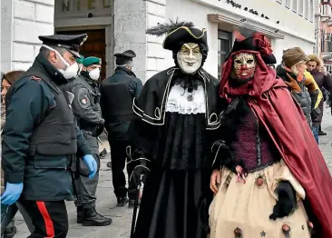  ?? AP ?? A policeman wearing a sanitary mask passes by two revellers in Venice. Italian authoritie­s closed Venice’s famed carnival events in a bid to stop the spread of the novel coronaviru­s, as numbers of infected persons in the country soared to at least 152, the largest number of cases outside Asia.