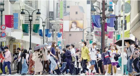  ?? — Reuters ?? Passers-by wearing protective face masks walk under the street decoration of Tokyo 2020 Olympic and Paralympic Games due to the coronaviru­s outbreak in Tokyo.