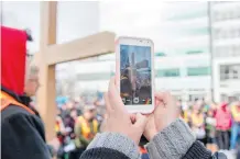  ??  ?? A woman uses her cellphone to snap a photo of the symbolic cross as the crowd carries it the city’s downtown on Good Friday. The Roman Catholic Diocese of Calgary organizes the annual event.