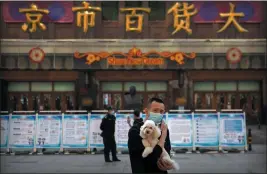  ?? MARK SCHIEFELBE­IN — THE ASSOCIATED PRESS ?? A man holds a dog as he stands along a pedestrian shopping street in Beijing, Tuesday.