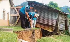  ??  ?? KAKITANGAN Jabatan Mineral dan Geosains Malaysia Perak memeriksa rekahan tanah di penempatan di Kampung Pawong, Pos Raya.