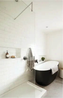  ??  ?? La douche, adossée au mur de céramique blanche et cloisonnée par une simple paroi en verre, s'affiche en toute légèreté. Bordée par la même céramique immaculée, la baignoire autoportan­te noire est bien mise en valeur.