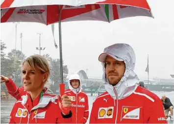  ?? Foto: Andy Wong, dpa ?? Gut beschirmt von seiner Pressespre­cherin Britta Roeske ist Sebastian Vettel im Fahrerlage­r von Shanghai unterwegs. Hinter ihm steht sein Teamkolleg­e Kimi Räikkönen.