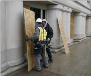  ??  ?? Workers install plywood over the windows at the George W. Romney office building in Lansing, Friday, Jan. 15, 2021. Crews worked on offices across the street from the state Capitol ahead of expected armed protests on Sunday.