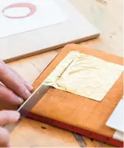  ??  ?? A square of gold leaf, held in place on a suede gilder’s cushion, is cut to size.