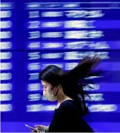  ?? ?? ▲A passerby walks past an electric monitor displaying recent movements of various stock prices outside a bank in Tokyo, Japan.