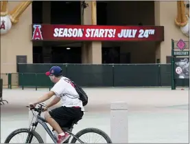  ?? ASHLEY LANDIS — THE ASSOCIATED PRESS ?? An Angels fan rides a bike past the entrance of Angels Stadium on Wednesday in Anaheim, Calif. The Angels and other Major League Baseball teams will report to their respective facilities for training this week, amid the coronaviru­s pandemic.