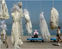  ?? AFP ?? A woman walks past a veiled woman sitting on a bench near an installati­on of wedding dresses by Lebanese artist Mireille Honein and Abaad NGO at Beirut’s Corniche. —