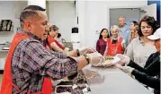  ??  ?? Volunteer Dominic Gonzales hands plates of food to other volunteers to be delivered to tables.