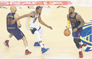  ??  ?? Cavaliers’ LeBron James controls the ball as Golden State Warriors’ Kevin Durant (centre) defence at the ORACLE Arena in Oakland, California. — AFP photo