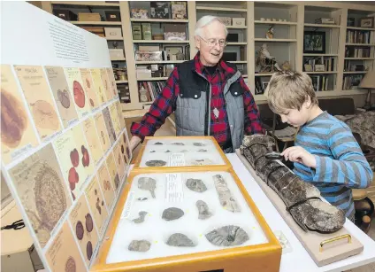  ??  ?? Tom Cockburn, chairman of the Victoria Palaeontol­ogy Society, and his nine-year-old grandson, Cayden Cockburn, look at a dinosaur’s femur and fossils, some of the items that will be on display at this weekend’s Fossil Fair.