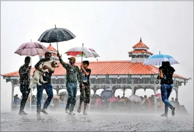  ??  ?? Pedestrian­s carry a dog as they make their way past others sheltering in a pavilion during a heavy monsoon rain downpour in Shimla on Wednesday. AFP