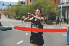  ??  ?? Monaghan, 23, checks his time on his watch before running through the winner’s ribbon at the finish line in Denver.