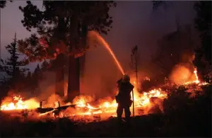  ?? The Associated Press ?? Firefighte­r Elroy Valadez sprays water over a spot fire from the Caldor Fire burning along Highway 89 near South Lake Tahoe, Calif.