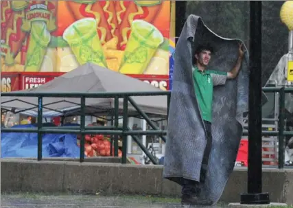  ?? MATHEW MCCARTHY, RECORD STAFF ?? Chris Wood tries to stay dry under a blanket during a downpour behind Waterloo City Hall, Thursday. Wood is part of the crew setting up the midway for the Busker Festival.