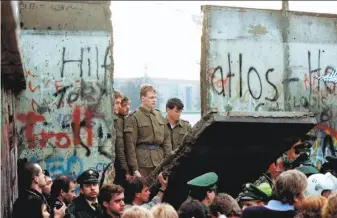  ?? Lionel Cironneau/ Associated Press ?? East German border guards watch as demonstrat­ors pull down a segment of the Berlin Wall in 1989. A nursing home tries to trigger such memories as a form of therapy for dementia.