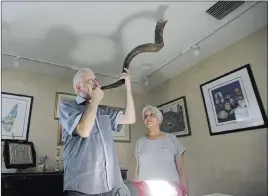  ?? Alan Diaz ?? The Associated Press Michael Andron blows the shofar as he prepares for Rosh Hashanah with his wife Lillian watching as they use a battery powered lantern to illuminate the room at their home Tuesday in Miami. The Androns have been without power for...