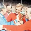  ?? AP ?? ENGLAND captain Bobby Moore, second right, with coach Alf Ramsey, left, as Nobby Stiles kisses the Jules Rimet Trophy. Stiles’ family is suing the FA following the football legend’s death in 2020. |