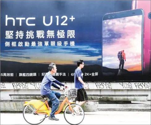  ?? AFP ?? People pass an advertisem­ent for Taiwan smartphone maker HTC in Taipei.
