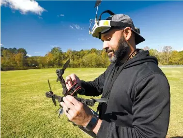  ?? STAFF PHOTO BY TIM BARBER ?? Clarence Buttram adjusts a camera lens before flying his freestyle racing drone recently on an open field in Rossville.