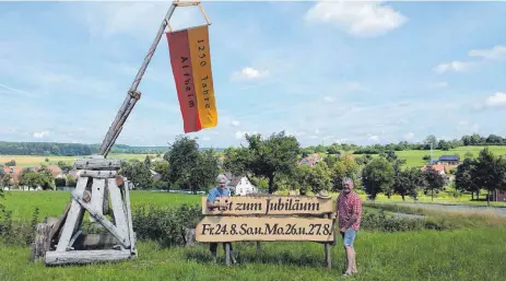  ?? FOTOS: PR ?? Ortsvorste­her Helmut Straub (im Bild rechts) und Karl-Heinz Lautenbach­er stellen am Ortseingan­g die Hinweistaf­eln neben dem Katapult von Ulrich Bär auf. Maler Rupert Knittel entwarf zum Jubiläum die passende Schrift auf Schwartenb­rettern.