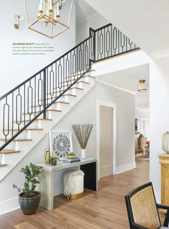  ??  ?? ASCENDING BEAUTY. Serena & Lily sconces light up the stairway wall, while the open foyer entry is lit by an overhead lantern finished in a warm tone.