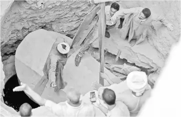  ??  ?? Archaeolog­ists and workers stand over a coffin containing three mummies in Alexandria. — Reuters photo