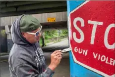  ?? Pittsburgh Post-Gazette ?? Kyle Holbrook, of Wilkinsbur­g, takes time out from painting a new mural to restore an older one June 22 in Homewood. Mr. Holbrook, Maghail Sahara and Ernest Bey created the original mural in 2007. Its message remains the same: Stop Gun Violence and Peace over Pittsburgh.