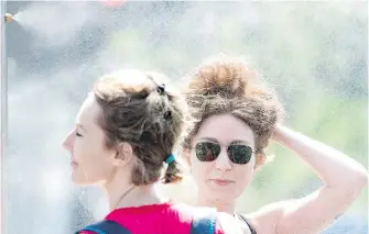  ??  ?? Two women take advantage of a light mist sprayed at a Montreal park this week.