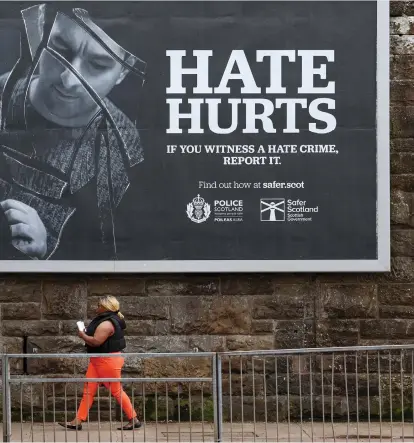 ?? ?? A member of the public walks past a billboard in Glasgow encouragin­g people to report hate crimes