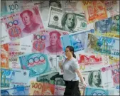  ?? KIN CHEUNG — THE ASSOCIATED PRESS FILE ?? A woman walks by a money exchange shop decorated with different countries currency banknotes at Central, a business district in Hong Kong.