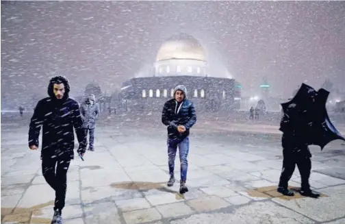  ?? Agence France-presse ?? ↑ Palestinia­ns leave as snow falls on the Dome of the Rock Mosque in Jerusalem on Wednesday.