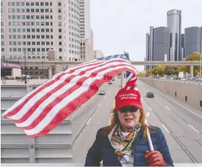  ?? SETH HERALD / AFP VIA GETTY IMAGES ?? A supporter of U.S. President Donald Trump stands with a flag over a freeway near the TCF Center in downtown Detroit. Former vice-president
Joe Biden was closing in on victory as night drew near on Thursday.