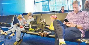  ?? Robert Alexander
Getty Images ?? A MAN AND HIS CHILDREN use their smartphone­s, tablets and other mobile devices as they wait for their f light in the boarding gate area at LaGuardia Airport in New York City.