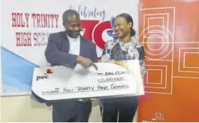  ?? ?? Gail Moore, partner and environmen­t lead at PWC Jamaica presents a symbolic cheque for $2.1 million to Father Carl F Clarke, principal at Holy Trinity High School.