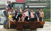  ?? — AFP ?? People ride in the front of a wheel loader to cross a flooded street following heavy rains in the city of Zhengzhou in China’s Henan province on Friday.