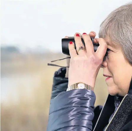  ??  ?? > Theresa May watches birds from inside a bird hide with schoolchil­dren at the London Wetland Centre yesterday after