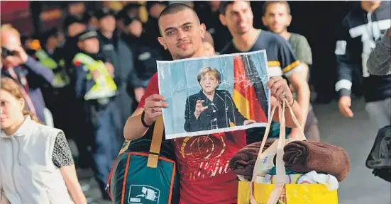  ?? SVEN HOPPE / EFE ?? Un refugiat sirià acabat d’arribar a l’estació de ferrocarri­l de la ciutat alemanya de Munic ensenya content un retrat de la cancellera Merkel