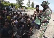  ?? (AP/Riza Azhari) ?? An Indonesian soldier inspects the identifica­tion of Rohingya men on Sunday after they land on a beach in Pidie, Aceh province, Indonesia.