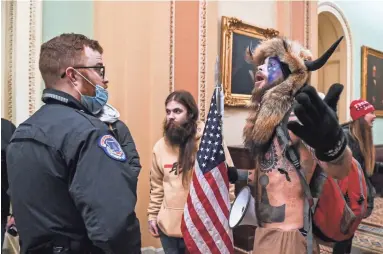  ?? GETTY IMAGES ?? U.S. Capitol Police officers try to stop supporters of President Donald Trump, including Jake Angeli, right, a QAnon supporter known for his painted face and horned hat, from entering the Capitol on Wednesday.