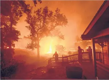  ?? NOAH BERGER/AP ?? In a year marked by climate-related disasters worldwide, five of the six largest wildfires in California’s history happened in 2020. Above, people watch as flames approach a home Aug. 21 in incorporat­ed Napa County.