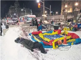  ?? JUSTIN TANG THE CANADIAN PRESS ?? A man rests on a snowbank in downtown Ottawa. Both the House and the Senate cancelled their Friday sessions on over security concerns as police began to clear protesters.