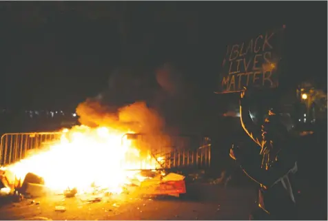  ?? — REUTERS ?? A man in Washington, D.C., holds a sign near a fire during a protest Sunday amid nationwide unrest in the U.S. following the death in Minneapoli­s police custody of George Floyd.